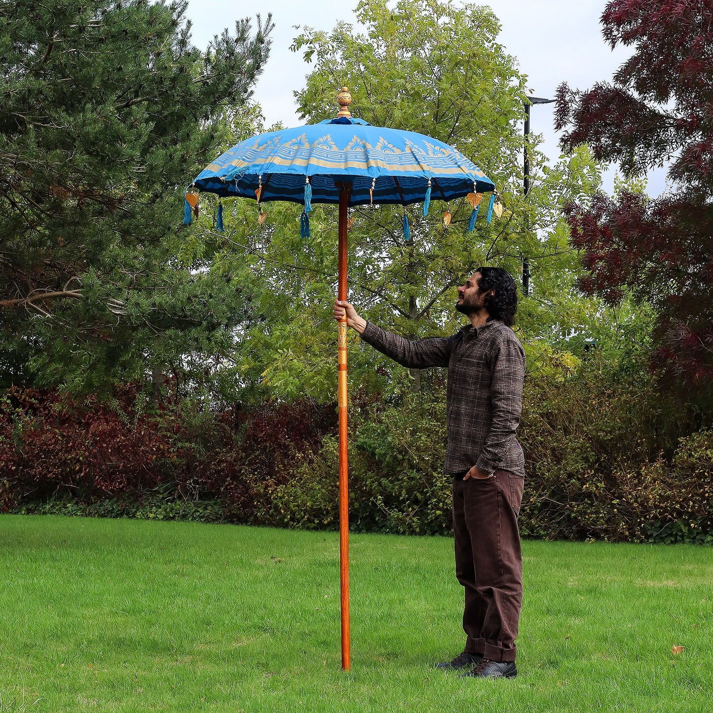 Handmade turquoise cotton patio parasol featuring intricate gold motifs and decorative tassels on a wooden pole.
