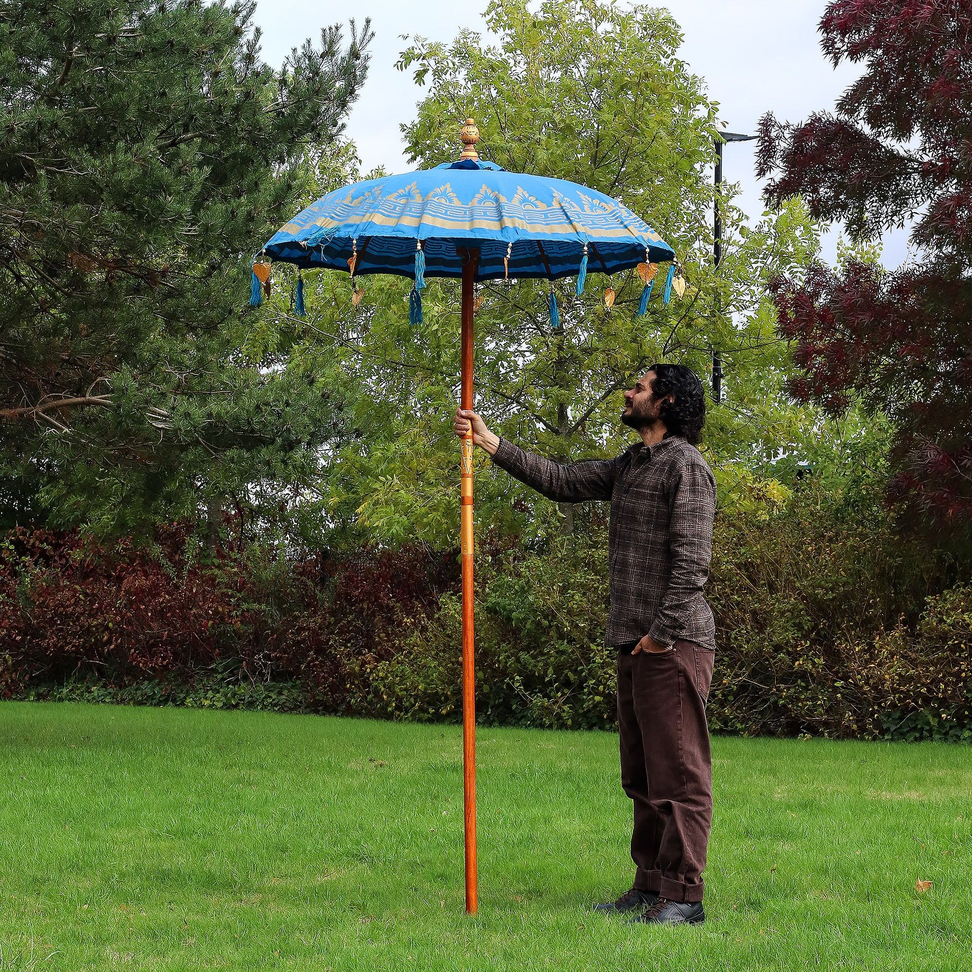 Handmade turquoise cotton patio parasol featuring intricate gold motifs and decorative tassels on a wooden pole.