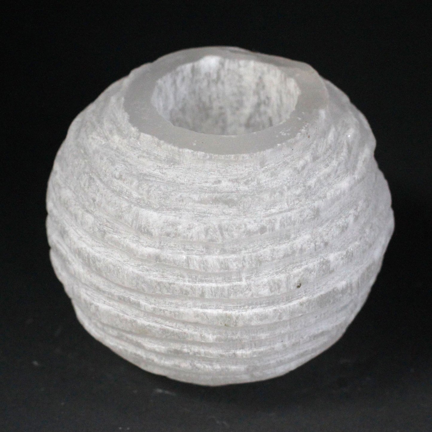 Round white selenite candle holder with a rough natural texture and a hollow centre for a tea light candle.
