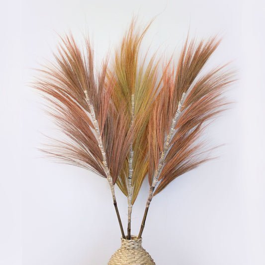 Tall dried Rayung grass stems in a vibrant coral pink, hand-braided onto vertical bamboo sticks for home decor.