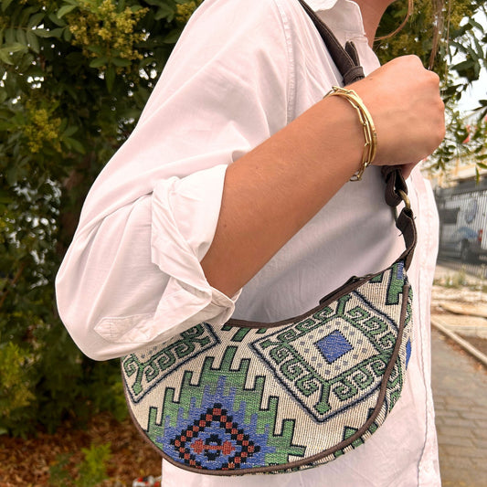 Intricately woven jacquard hobo bag featuring a geometric green and earthy pattern with a sturdy brown shoulder strap.