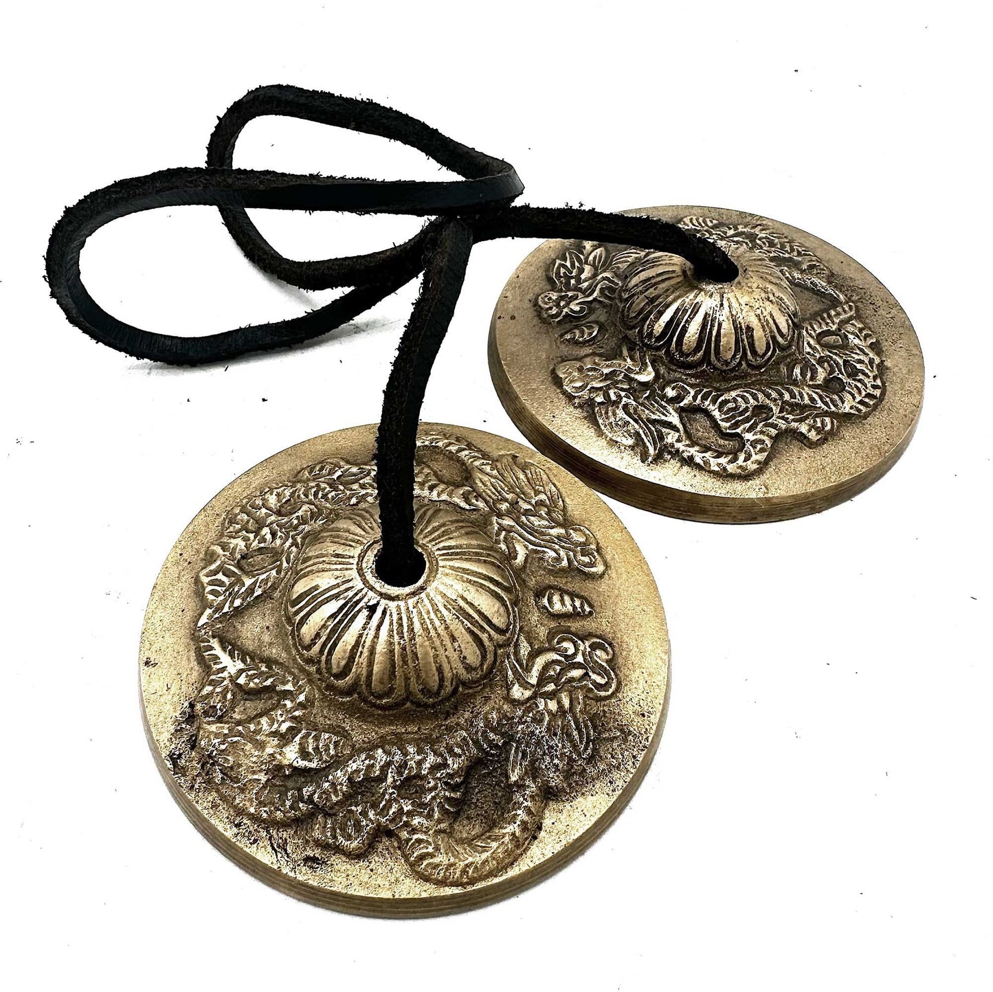 Two small handcrafted bronze cymbals embossed with traditional dragon designs, connected by a leather strap.