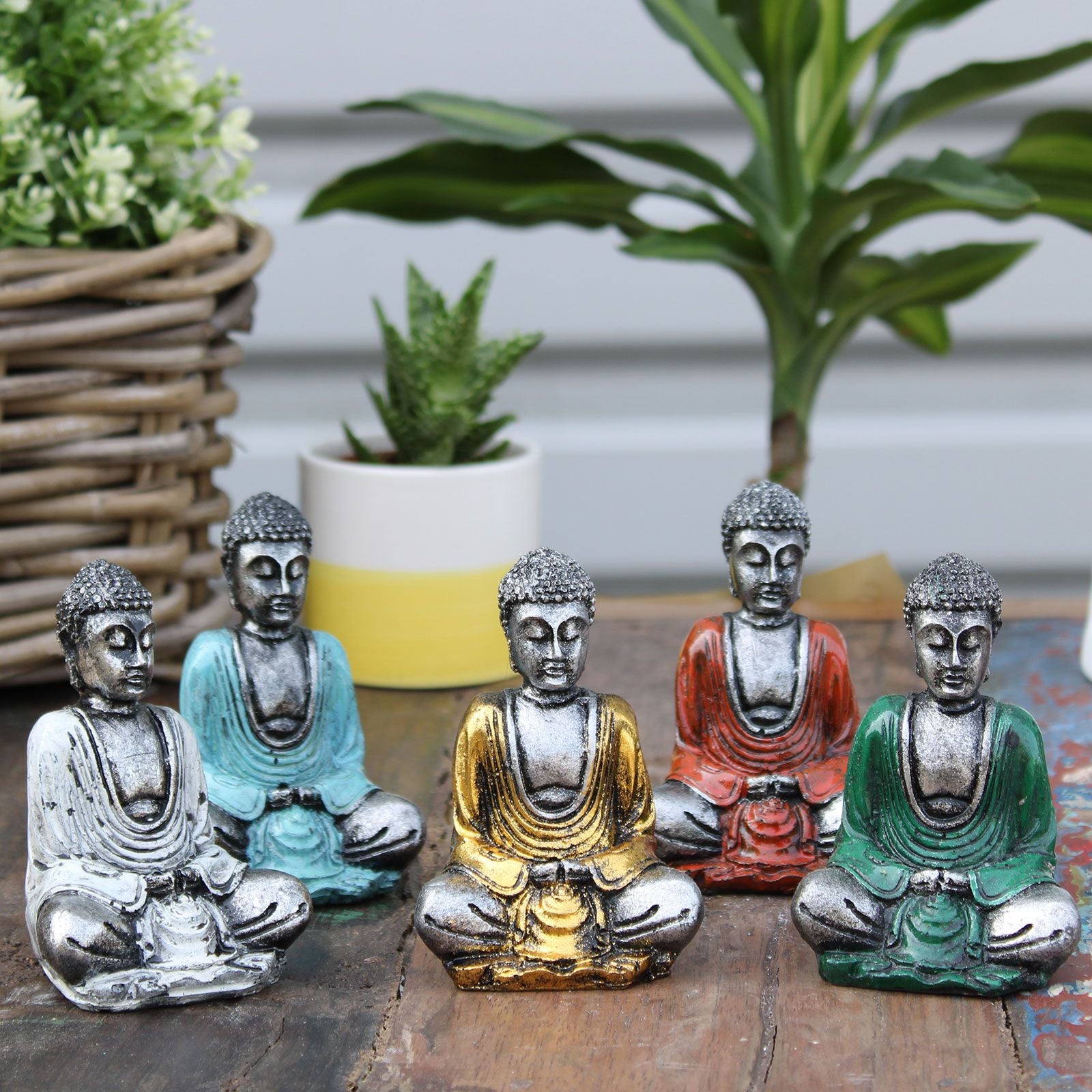 Set of six small silver-coloured resin Buddha figurines in various meditative poses on a plain surface.