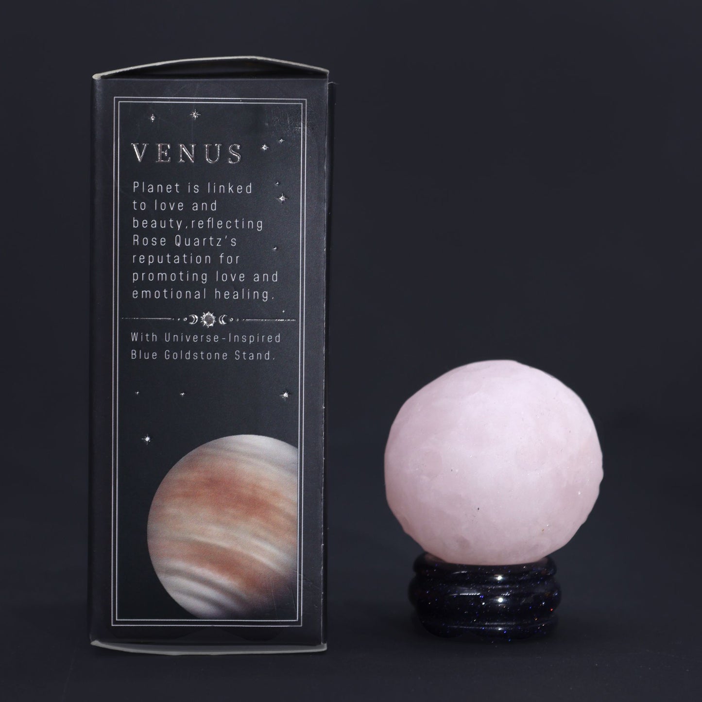 A polished pink rose quartz sphere resting on a glittering dark goldstone pedestal stand.