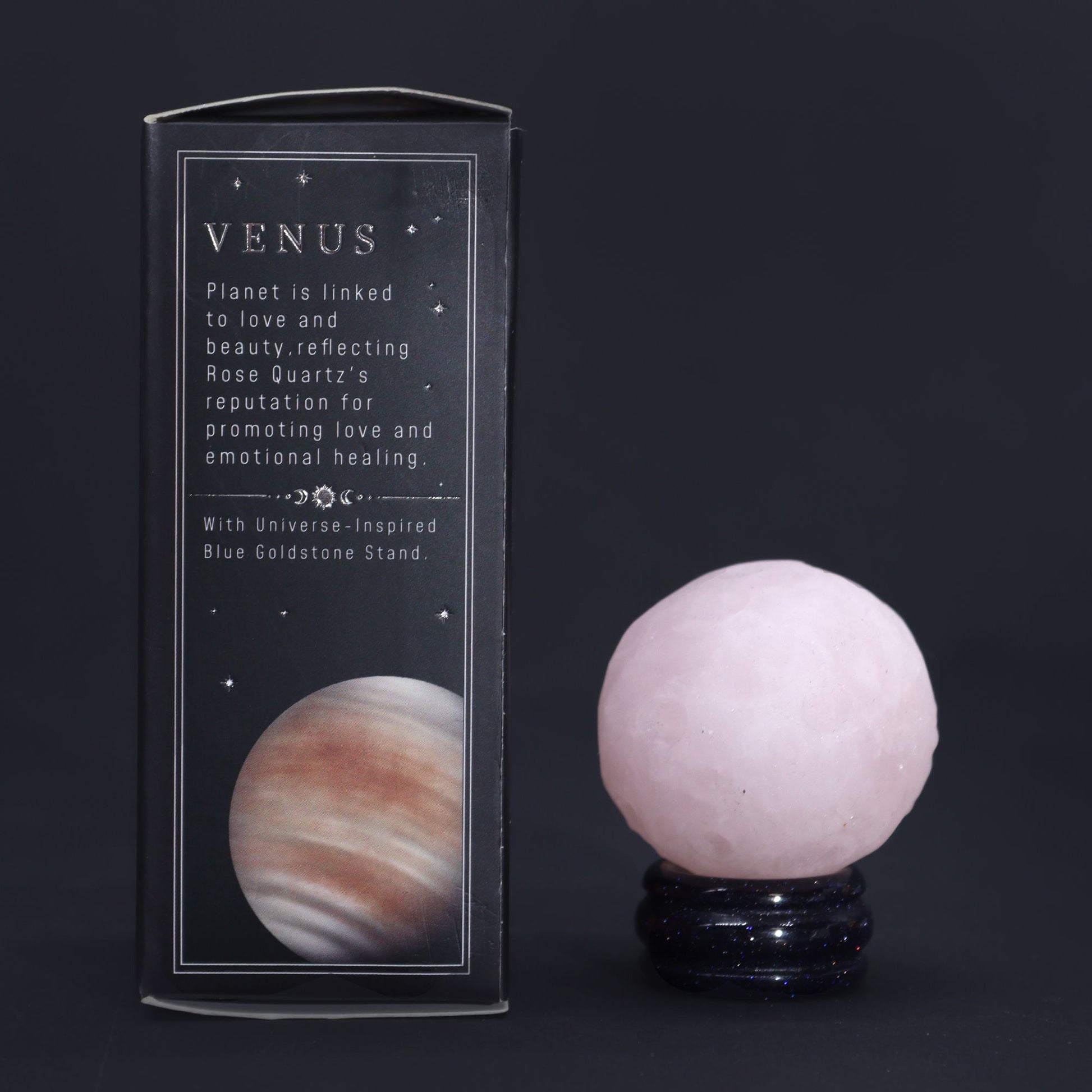 A polished pink rose quartz sphere resting on a glittering dark goldstone pedestal stand.
