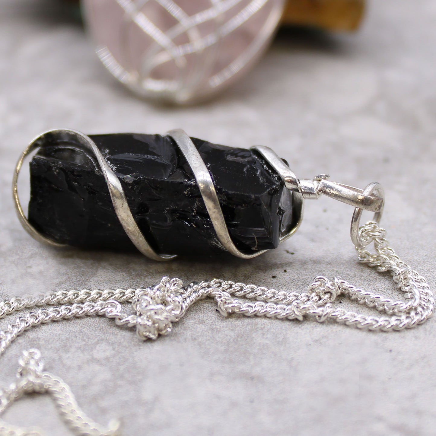 Rough black onyx gemstone pendant wrapped in silver-coloured wire on a delicate necklace chain.