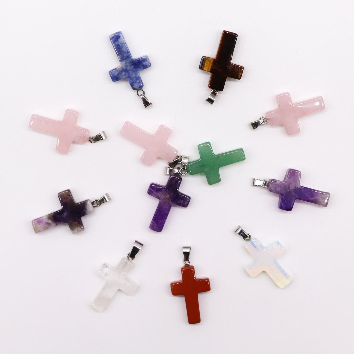Twelve assorted colourful gemstone pendants carved into small cross shapes with silver-tone bails.
