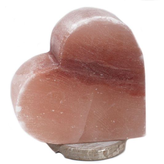 Hand-carved heart-shaped pink Himalayan salt lamp glowing with a warm orange light on a wooden base.