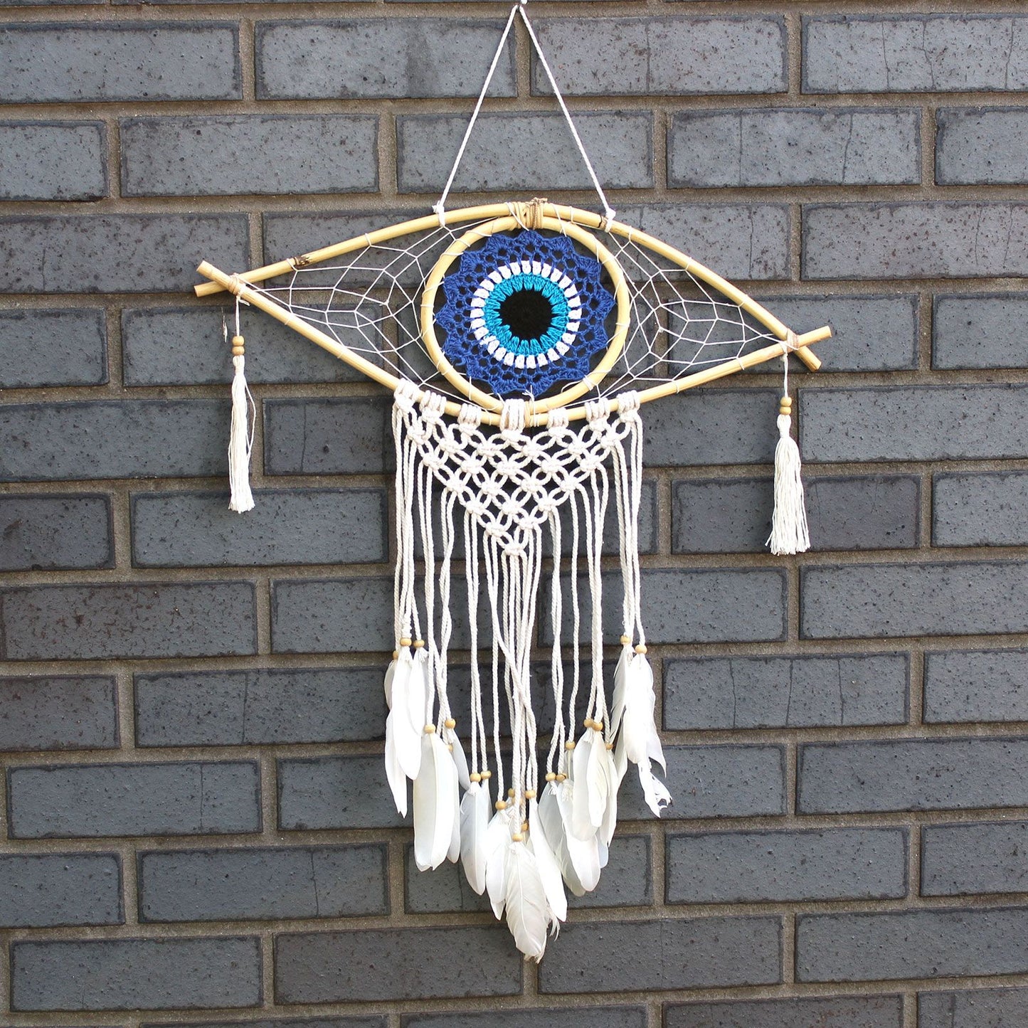 Medium macrame dream catcher featuring a central blue, white, and black evil eye design with woven cotton fringing.