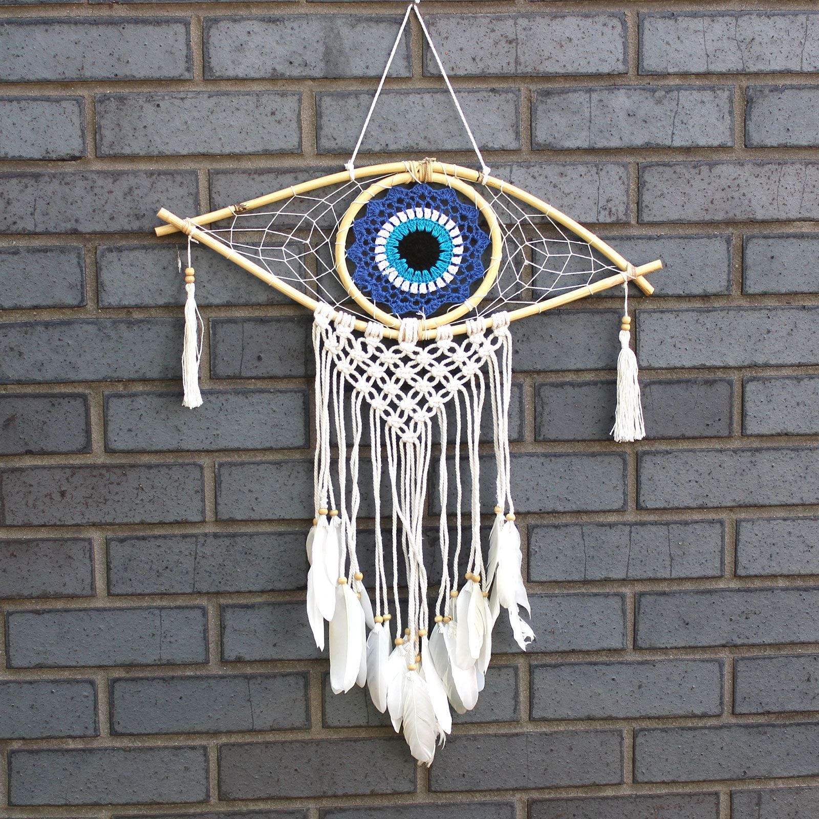 Medium macrame dream catcher featuring a central blue, white, and black evil eye design with woven cotton fringing.