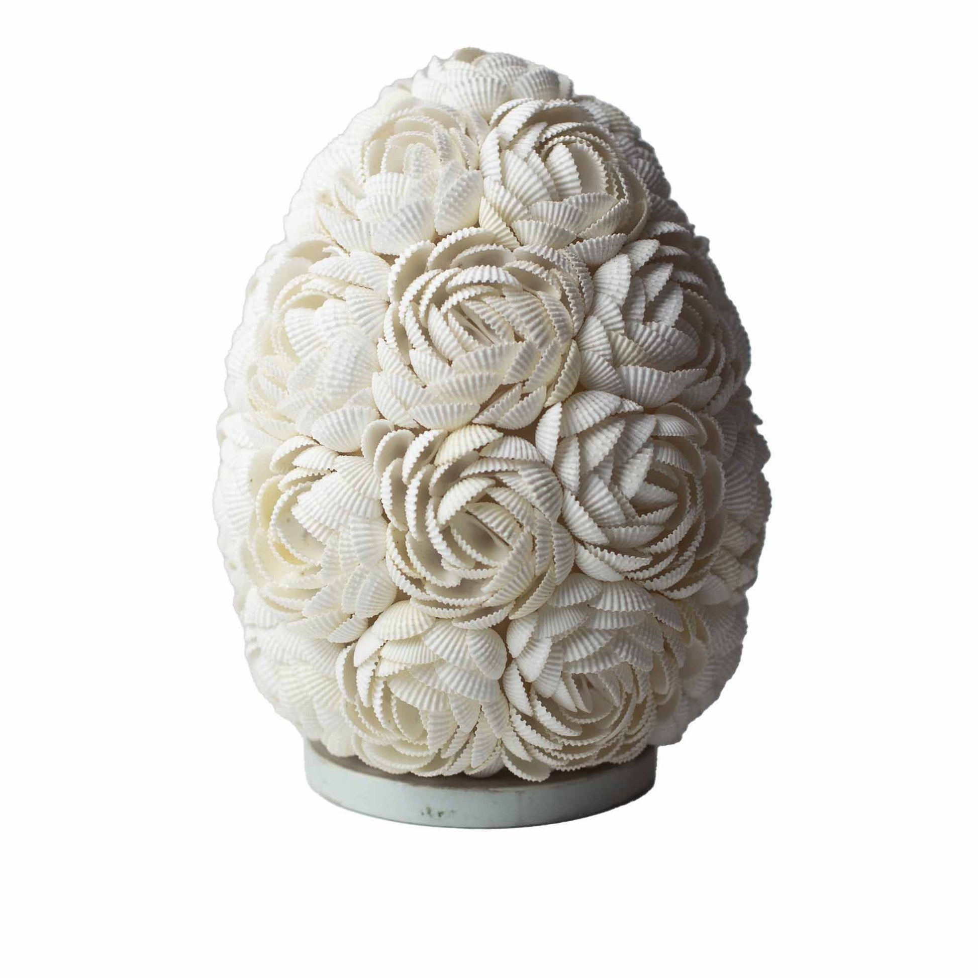 Handcrafted oval lamp covered in natural rose-toned seashells emitting a warm and inviting atmospheric glow.