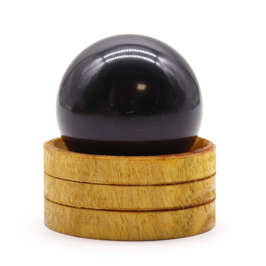 Polished black tourmaline crystal sphere on a simple wooden stand against a neutral background.