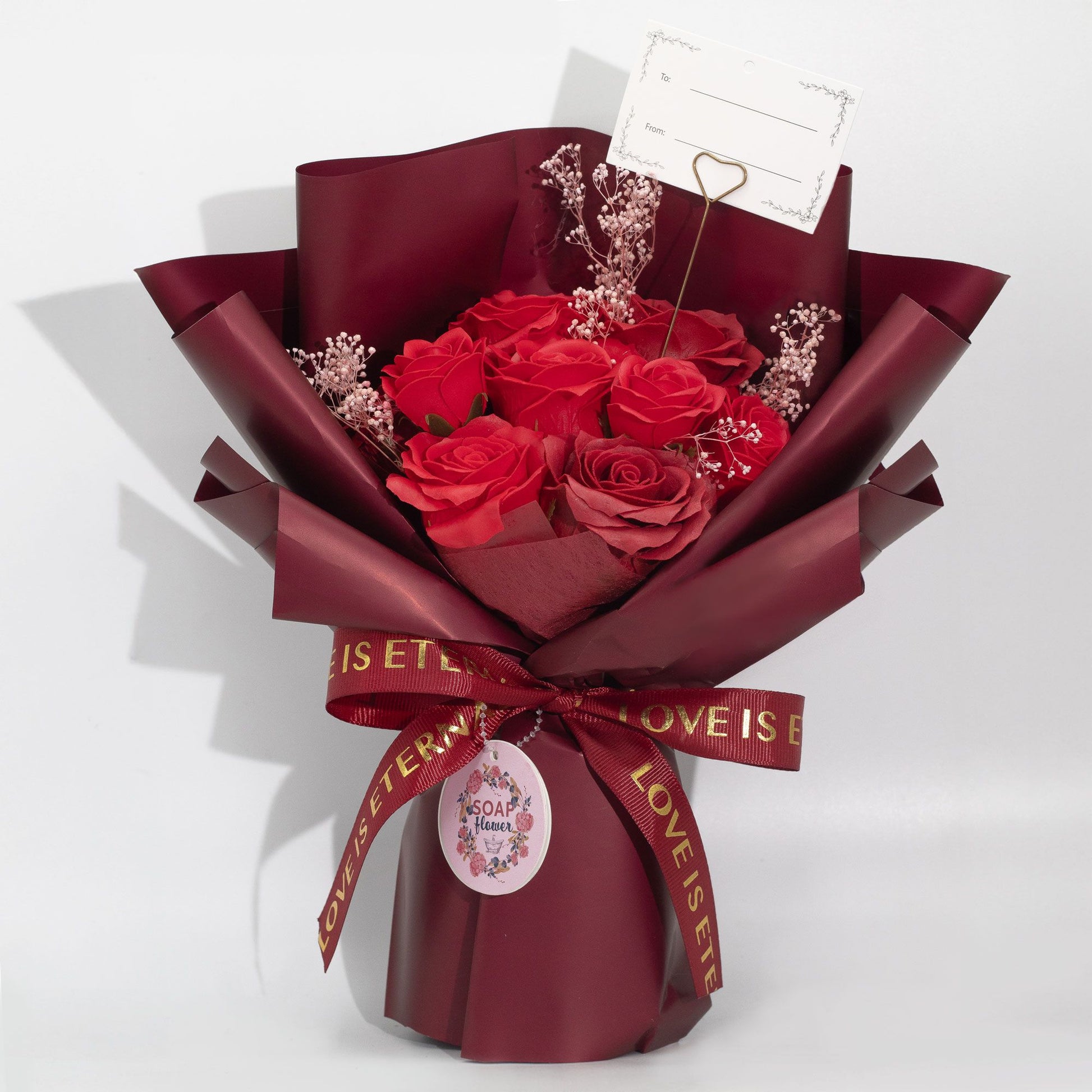 Large bouquet of realistic red soap roses wrapped in deep wine paper with a Love is Eternal satin ribbon.