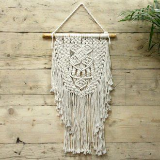 Intricate handcrafted cream macrame wall hanging with a complex woven pattern and fringed edges on a wooden dowel.