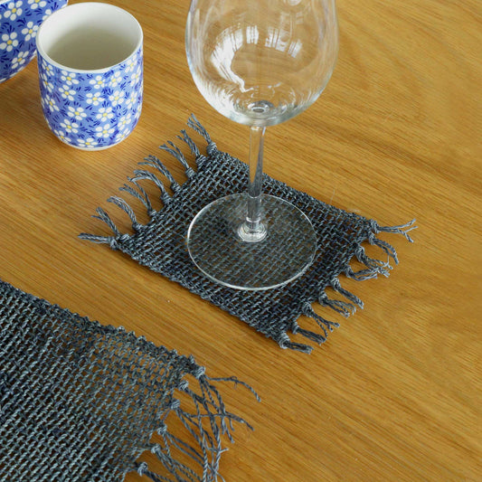 Set of four circular charcoal grey seagrass coasters featuring a decorative fringed edge on a neutral background.