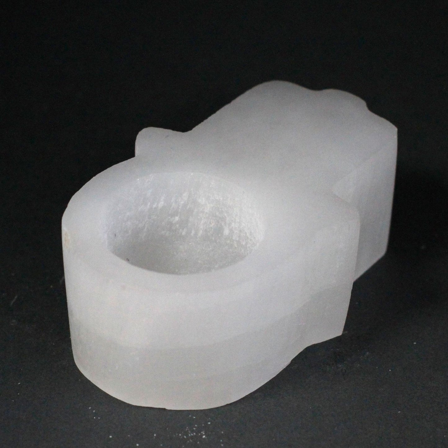 Carved white selenite candle holder in the shape of a Hamsa hand with natural rough edges and a translucent finish.