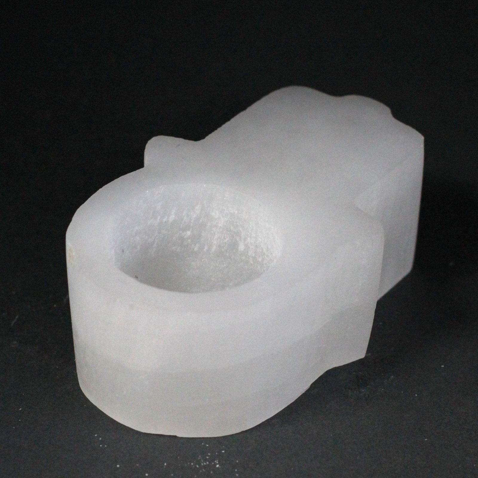 Carved white selenite candle holder in the shape of a Hamsa hand with natural rough edges and a translucent finish.