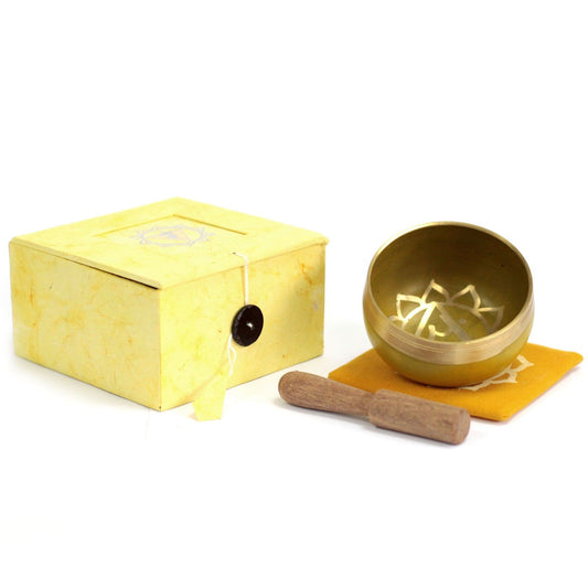 Handcrafted yellow chakra singing bowl with a wooden striker on a neutral background.