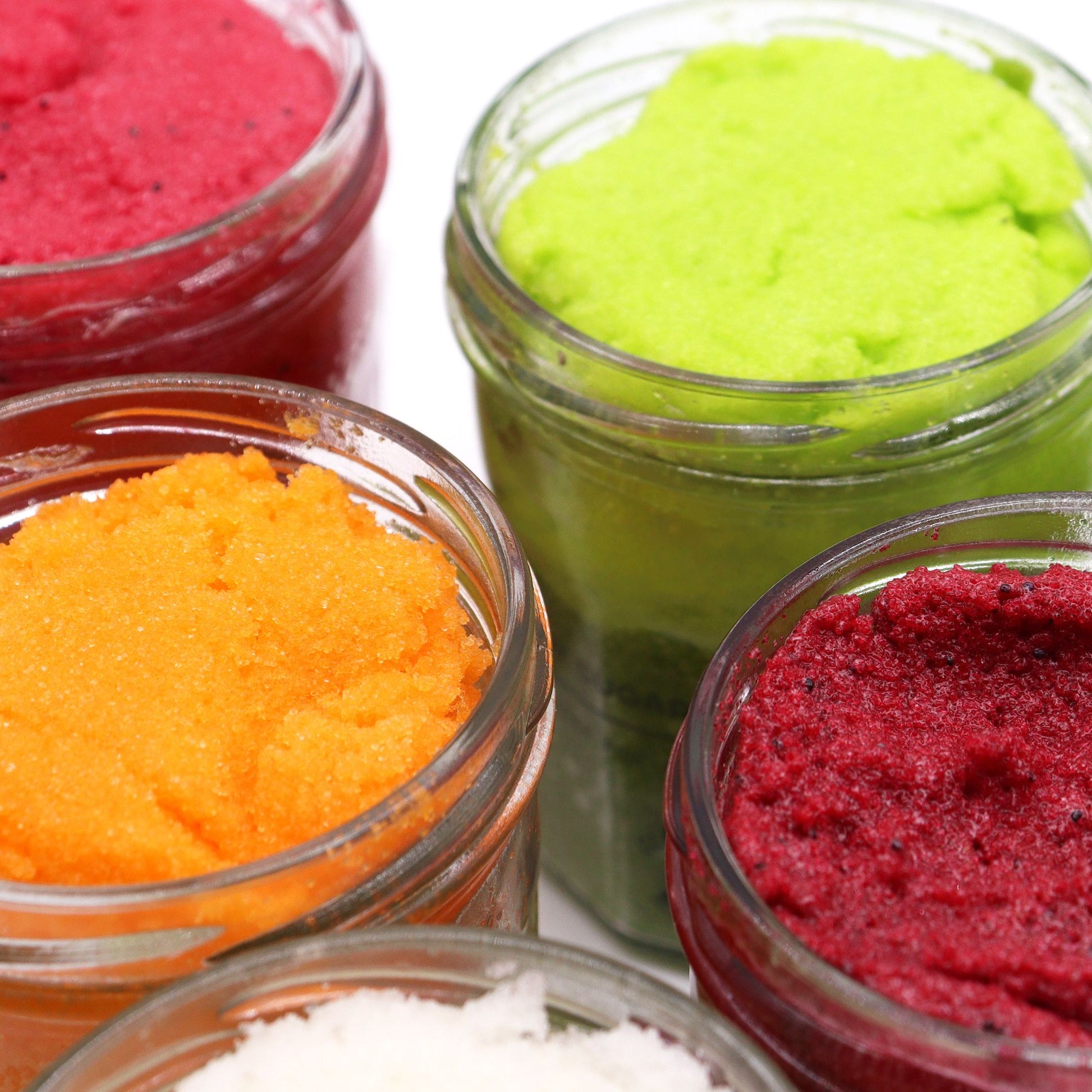 Close-up of a vibrant pink sugar body scrub in a clear jar, showing a rich, grainy exfoliating texture.