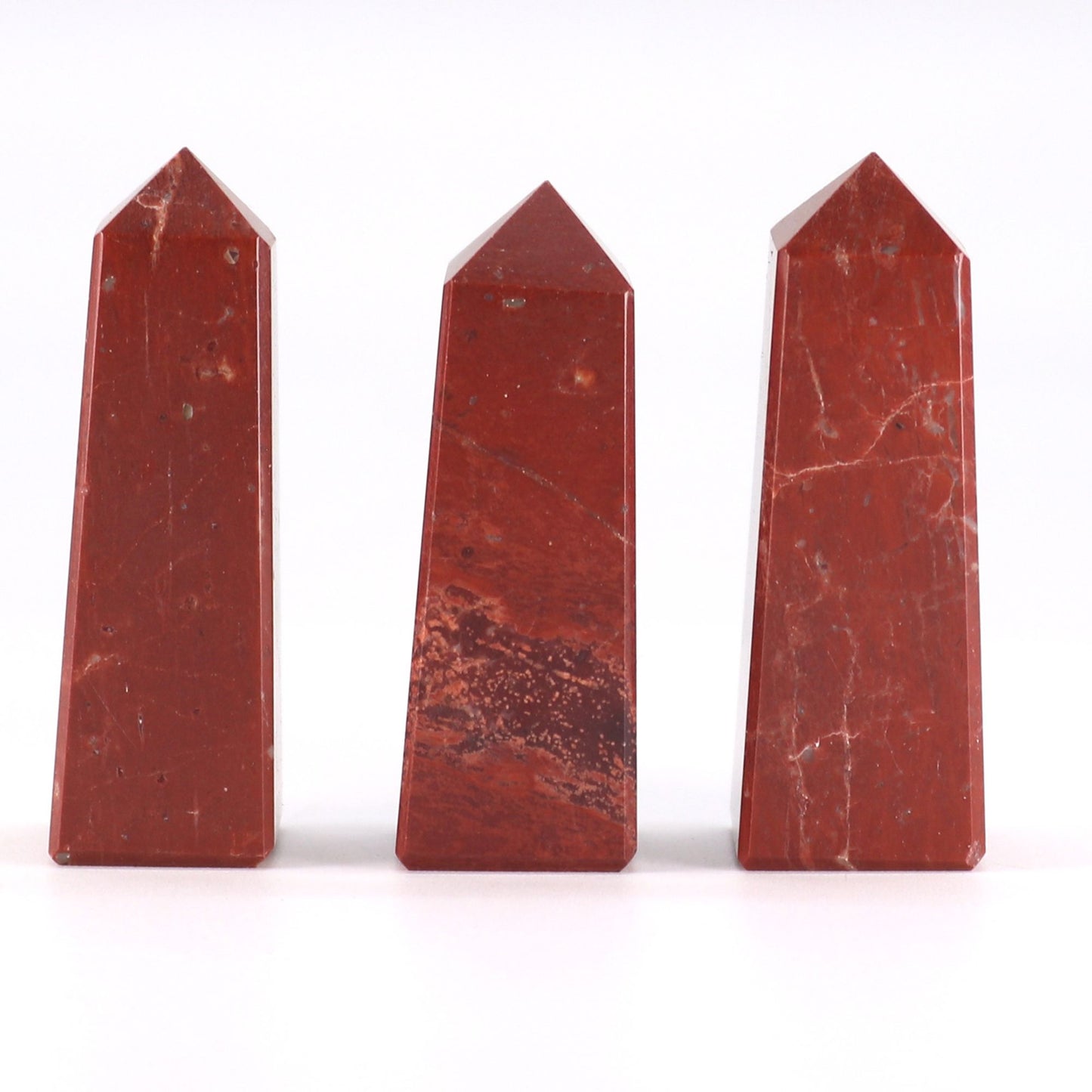Small polished red jasper gemstone obelisk point with a sharp tip and deep brick-red marbled patterns.