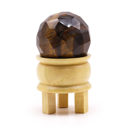Faceted Tigereye gemstone sphere resting on a small light brown wooden tripod stand.