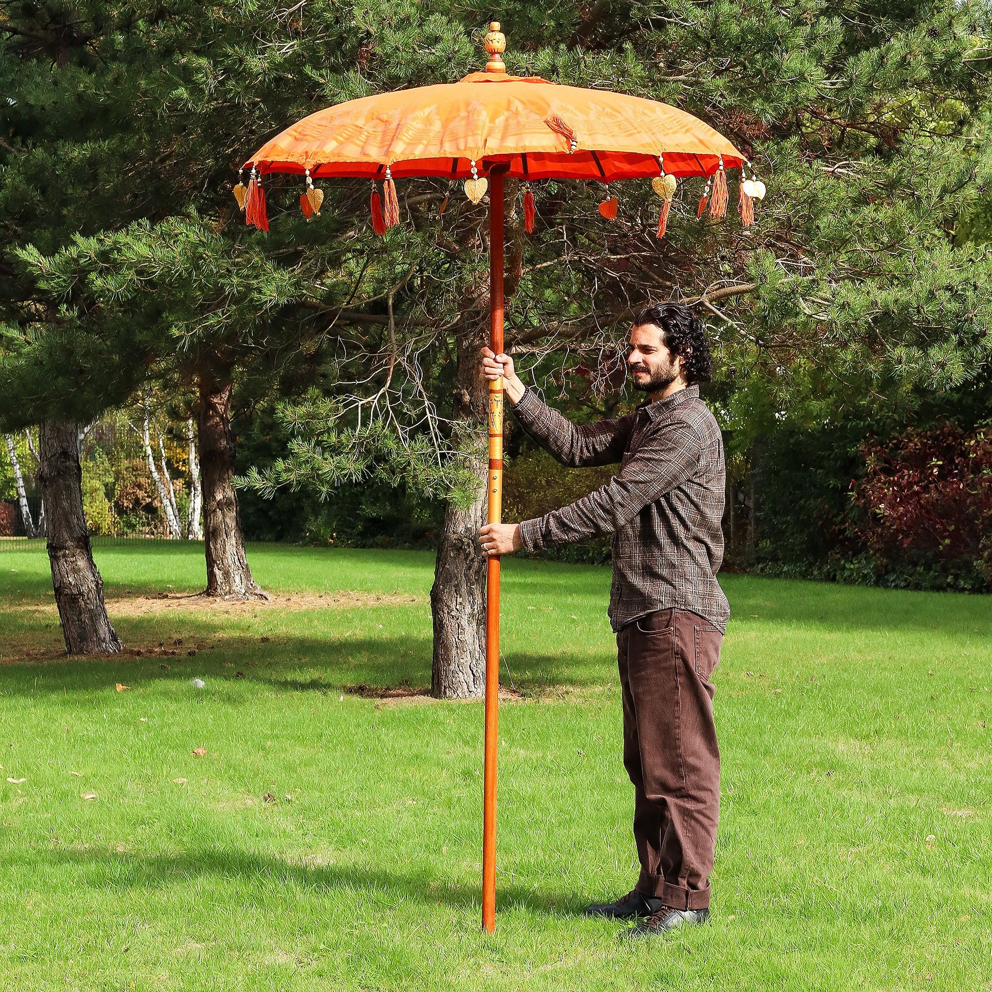 Vibrant orange cotton Bali patio parasol with ornate decorative hangings and traditional Indonesian craftsmanship.