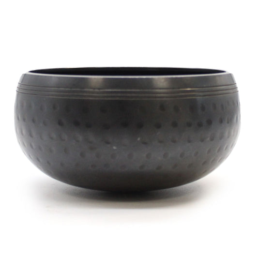 Small black beaten metal singing bowl with a textured surface resting on a flat base.