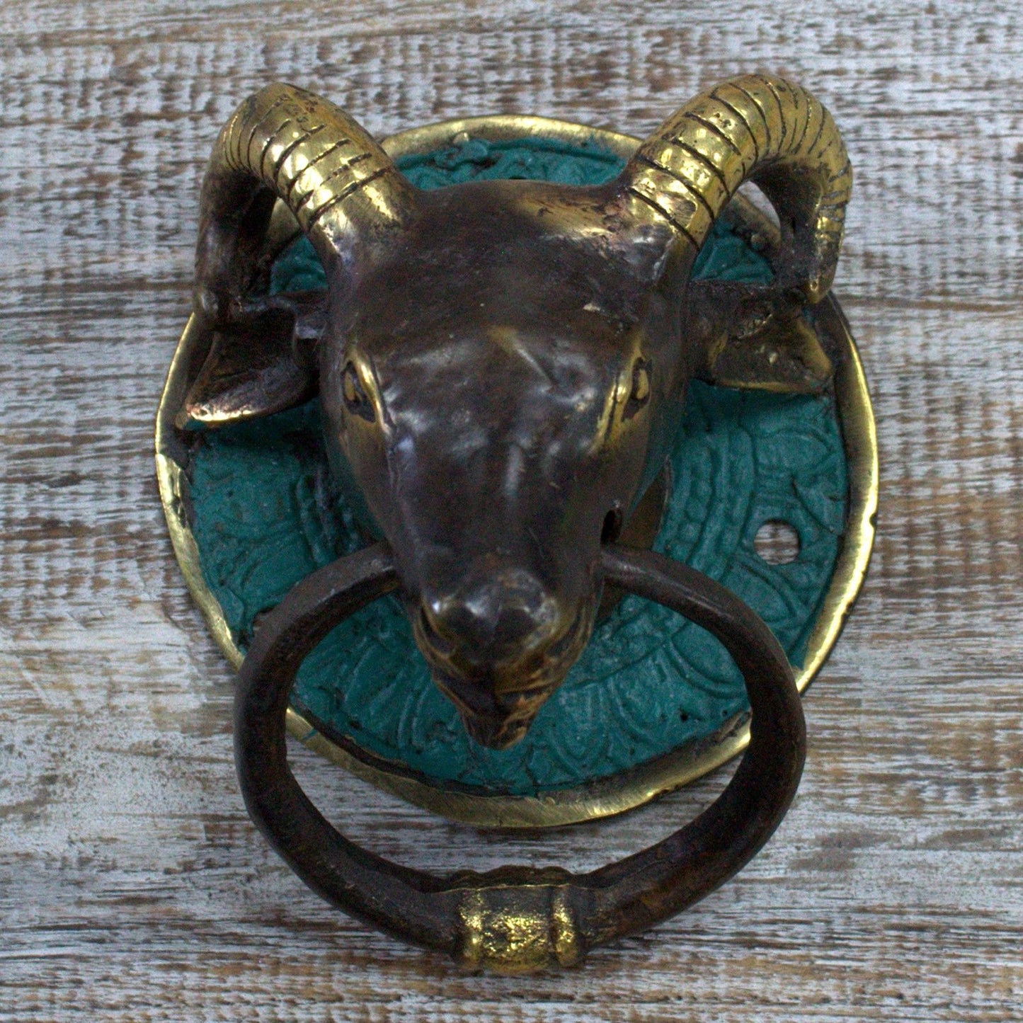 Intricate brass door knocker shaped like a ram's head with a textured finish and curved horns.
