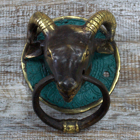 Intricate brass door knocker shaped like a ram's head with a textured finish and curved horns.