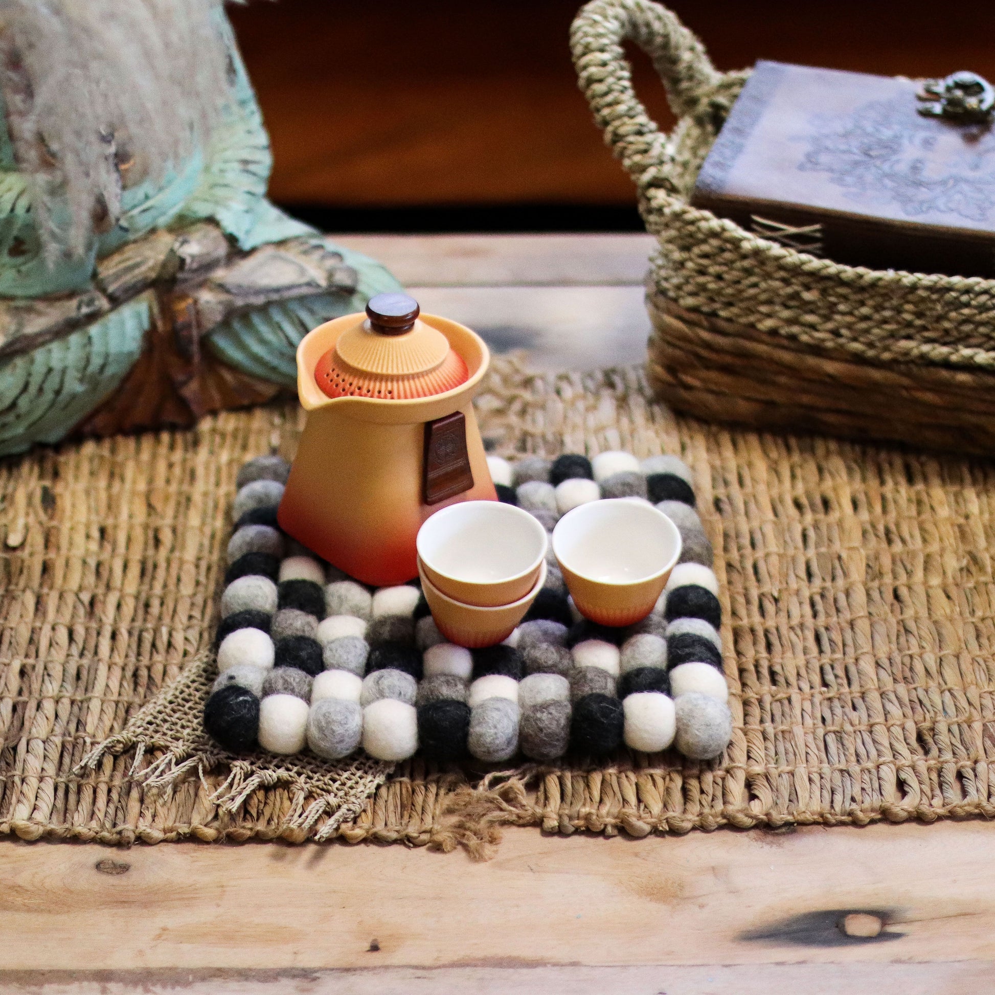 Handmade square placemat composed of numerous small wool felt balls in various shades of grey and charcoal.