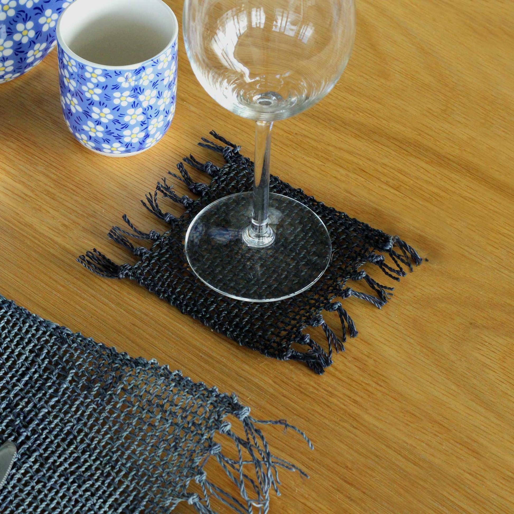 Set of four circular black seagrass coasters featuring a decorative fringed edge on a neutral background.