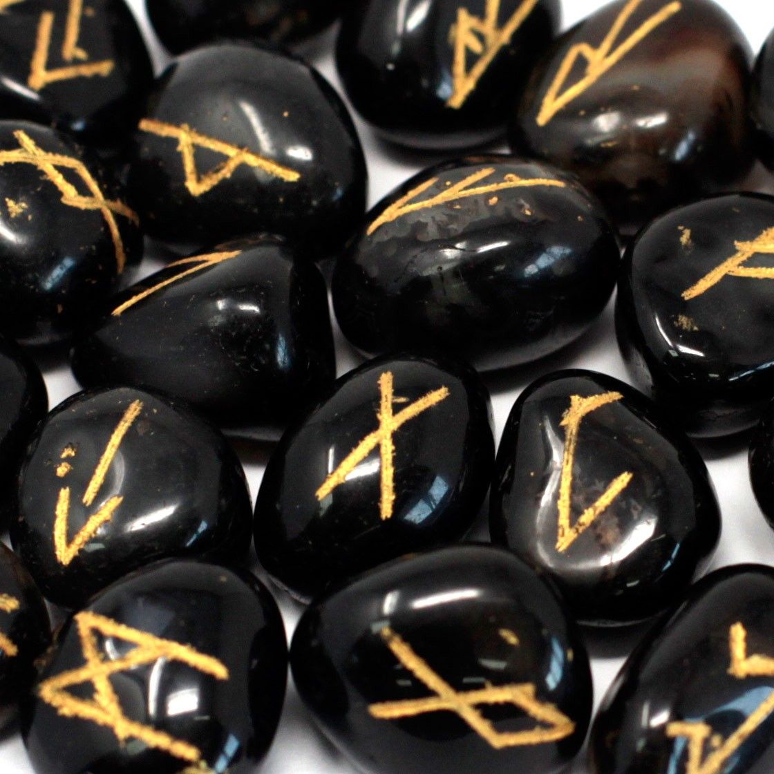 Polished black onyx rune stones with engraved gold lettering scattered next to a black drawstring pouch.