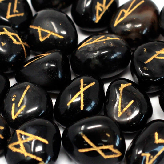 Polished black onyx rune stones with engraved gold lettering scattered next to a black drawstring pouch.
