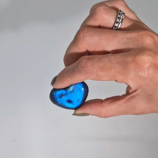 Heart-shaped labradorite gemstone showing iridescent blue and gold flashes against a dark grey crystalline surface.
