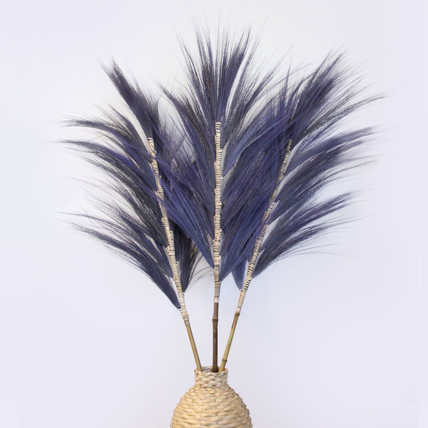 Tall lavender-dyed dried Rayung grass stems braided onto a bamboo stick against a neutral background.