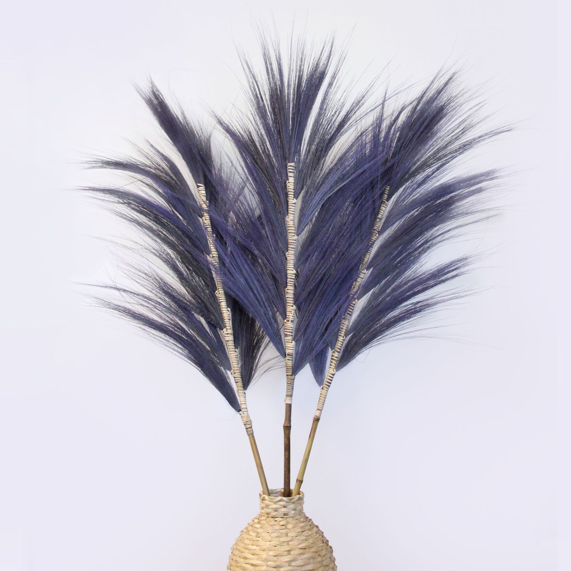 Tall lavender-dyed dried Rayung grass stems braided onto a bamboo stick against a neutral background.