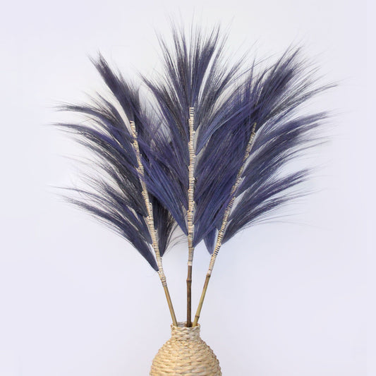 Tall lavender-dyed dried Rayung grass stems braided onto a bamboo stick against a neutral background.