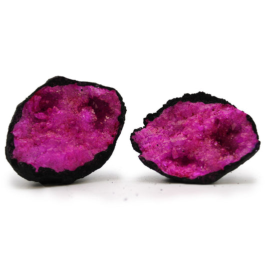 A cracked open black rock geode revealing vibrant artificially coloured dark red and pink calcite crystals inside.