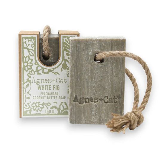 Handmade white fig soap on a natural rope hanging against a minimalist bathroom background.