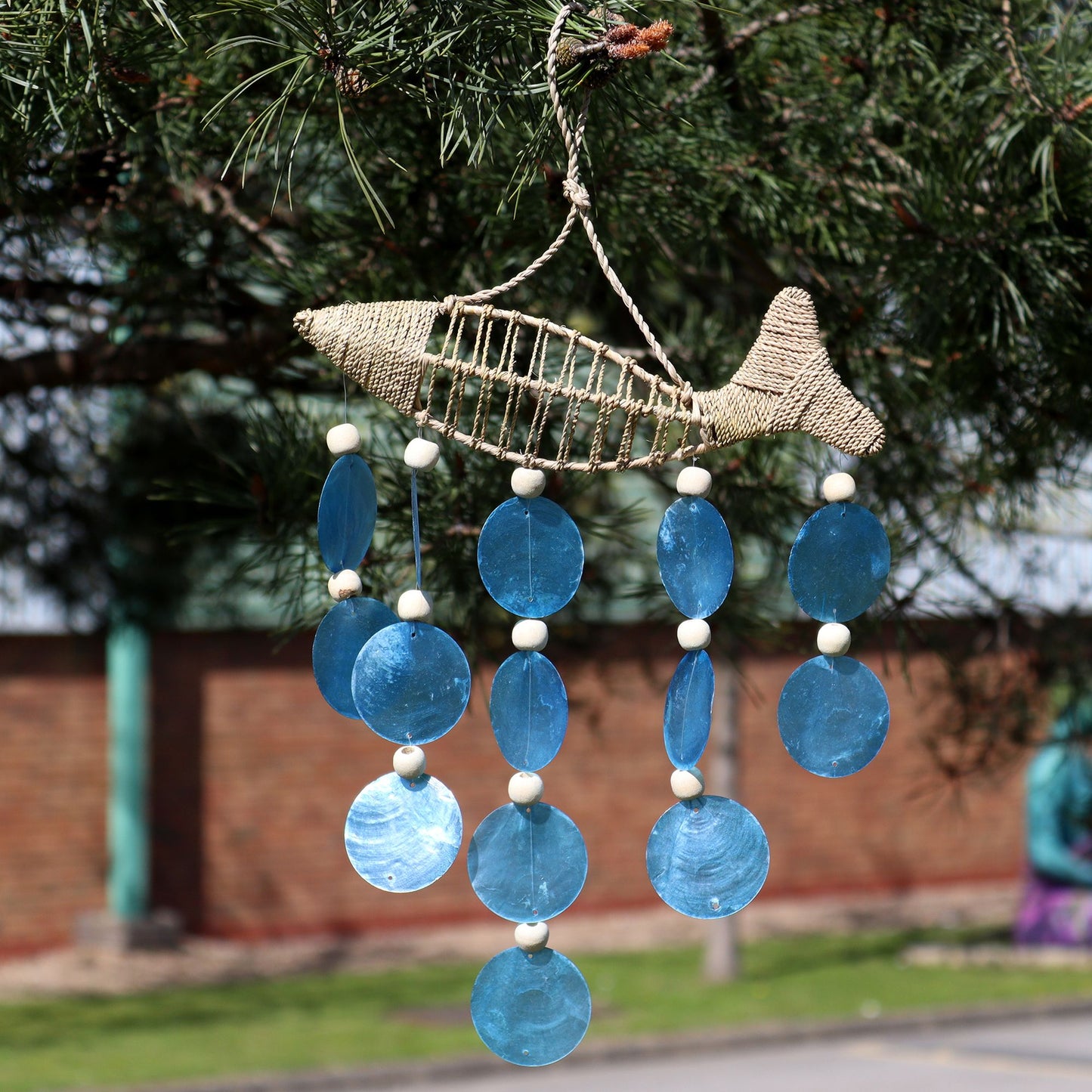 Coastal driftwood wind chime featuring hanging blue capiz shell drops and decorative wooden string fish.