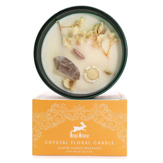Soy wax candle in a glass jar topped with dried flowers and a raw rock quartz crystal point.