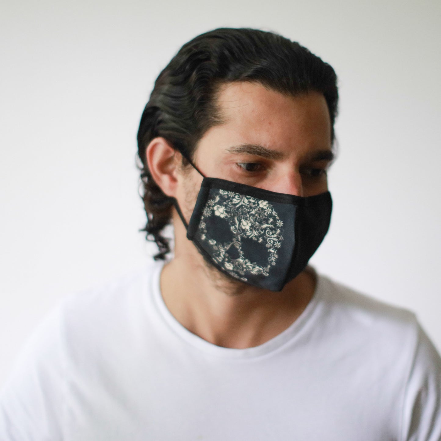 Close-up of a reusable fabric face mask featuring a vibrant colourful flower skull pattern on a dark background.