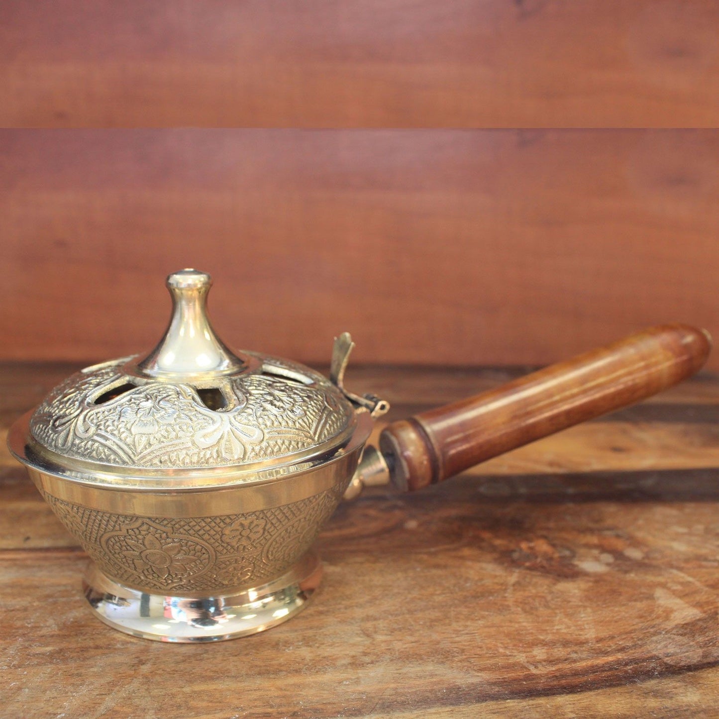 Intricately decorated brass incense censer with a wooden handle and vented lid for charcoal and resin burning.