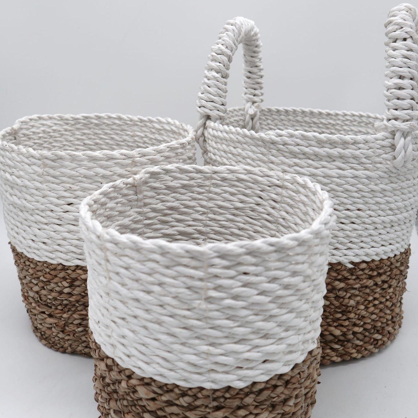 Set of three handwoven seagrass baskets with a natural and white two-tone design in varying sizes.