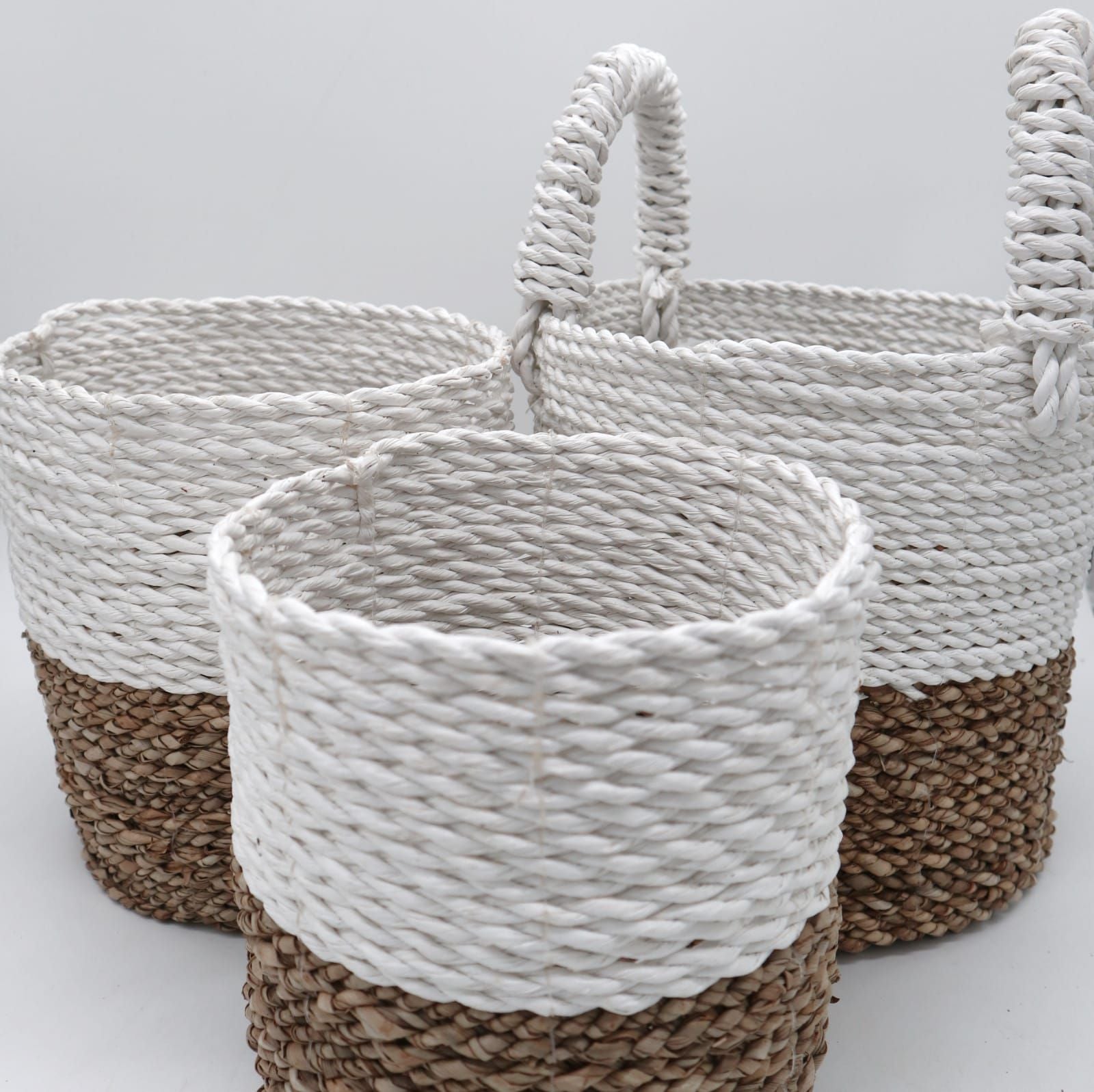 Set of three handwoven seagrass baskets with a natural and white two-tone design in varying sizes.