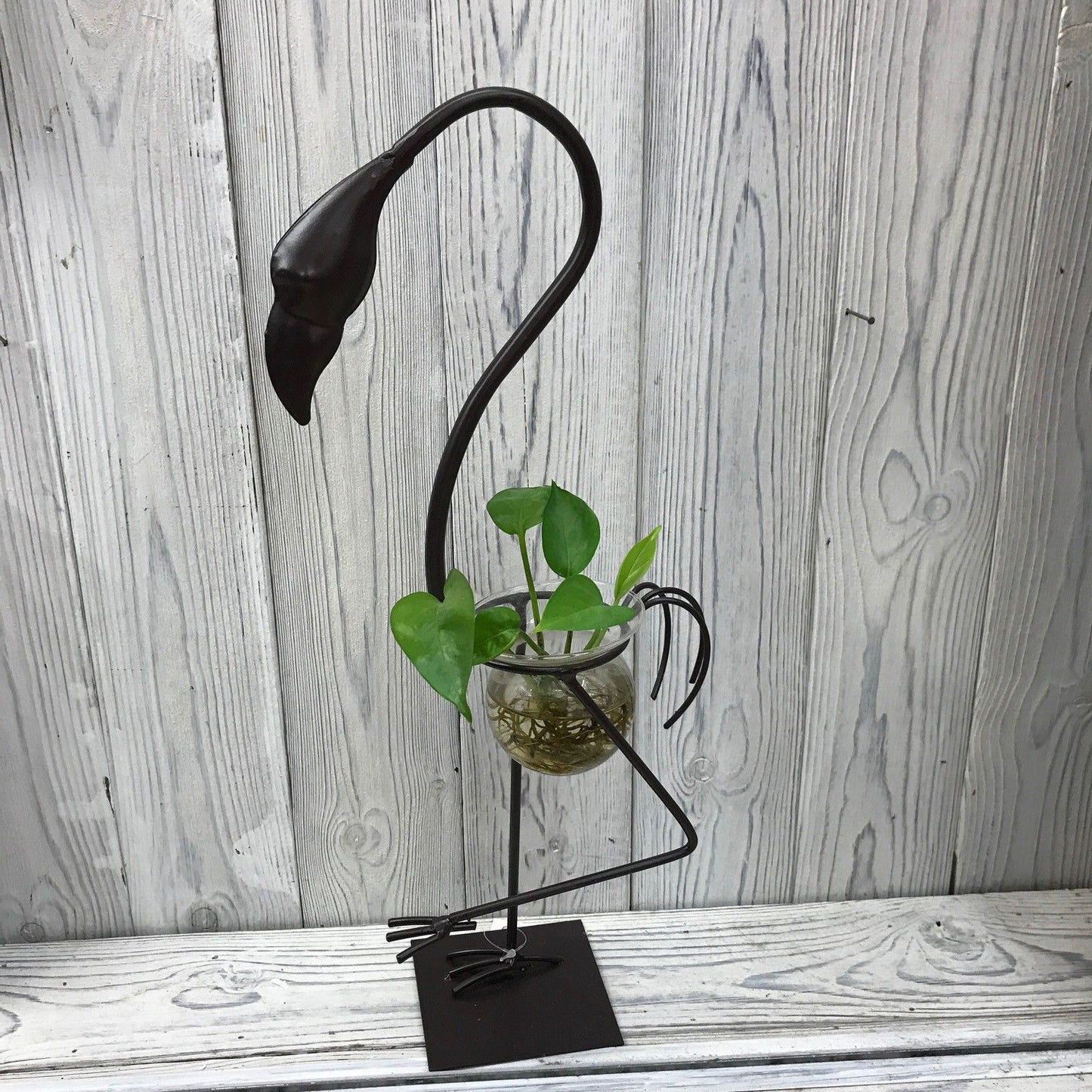 Tall pink metal flamingo stand holding a clear laboratory-style glass bulb for hydroponic plant display.