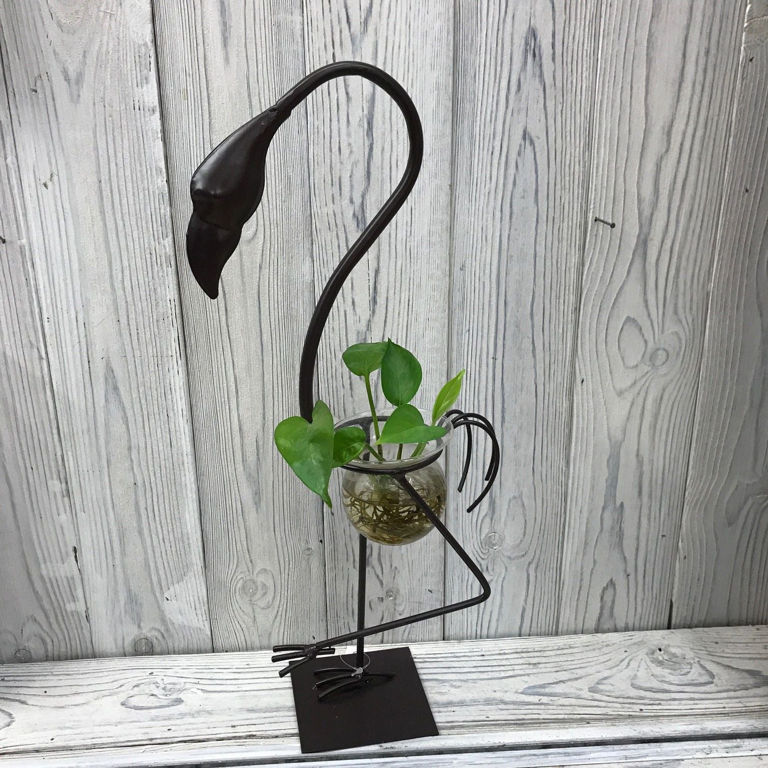 Tall pink metal flamingo stand holding a clear laboratory-style glass bulb for hydroponic plant display.