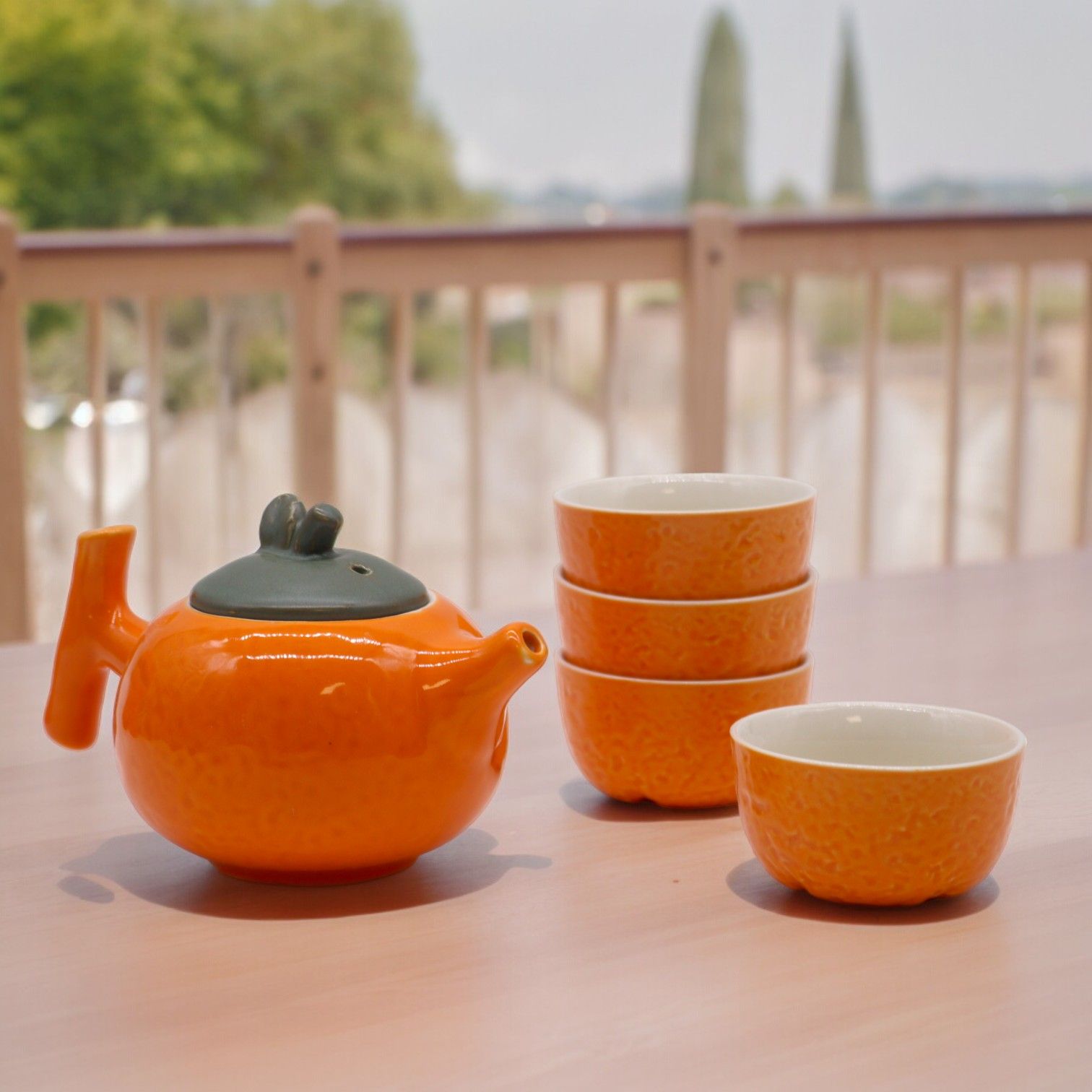 Vibrant orange ceramic teapot set with four matching cups, designed for brewing and serving herbal infusions.