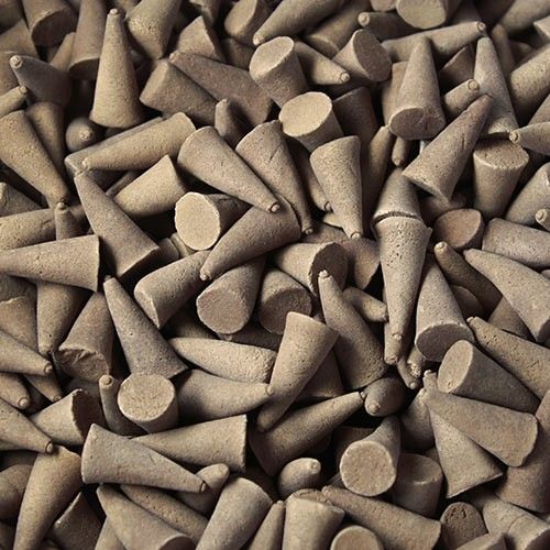 Large pile of aromatic dark brown patchouli incense cones on a neutral background.