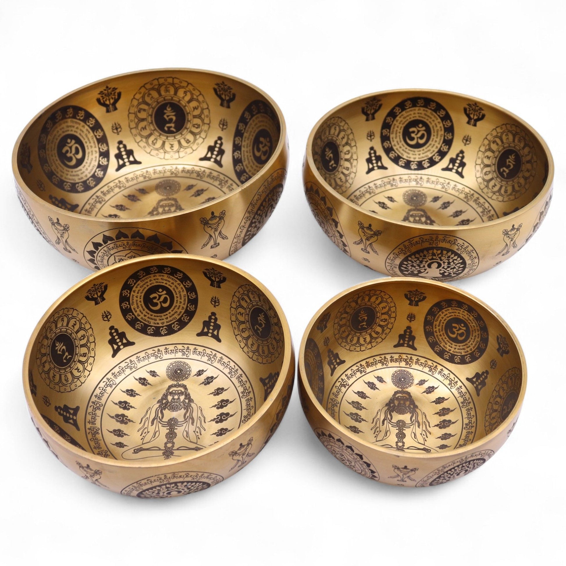 Set of four handcrafted brass singing bowls with intricate yogic etchings and spiritual symbols on a dark background.